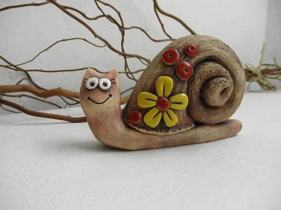 a snail figurine sitting on top of a white surface next to a tree branch