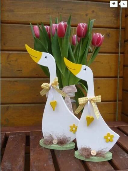 two white ducks sitting next to each other on top of a wooden table with tulips in the background