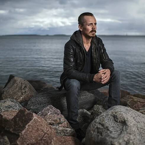 Finnish actor Jasper Pääkkönen sits on a rock in front of the Baltic Sea. 