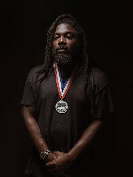 Jason Reynolds poses with his ambassador medal against a black background