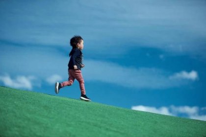 Young Asian boy running through a grassy field with blue skies in the background