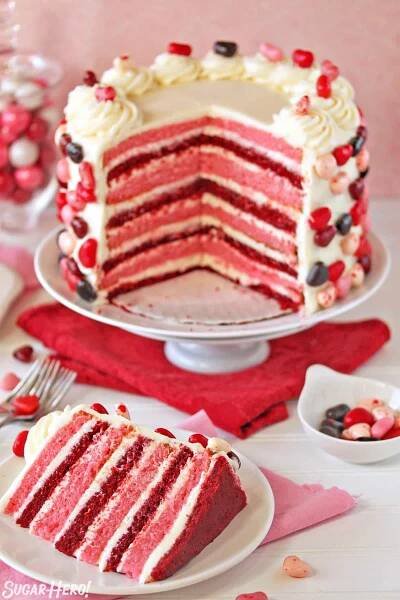 Pink and red velvet layer cake with several slices taken out, and a slice of cake displayed in front on a white plate.
