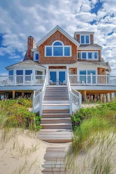Charming Cape Cod beach house with shingle siding and nautical decor, surrounded by coastal greenery.