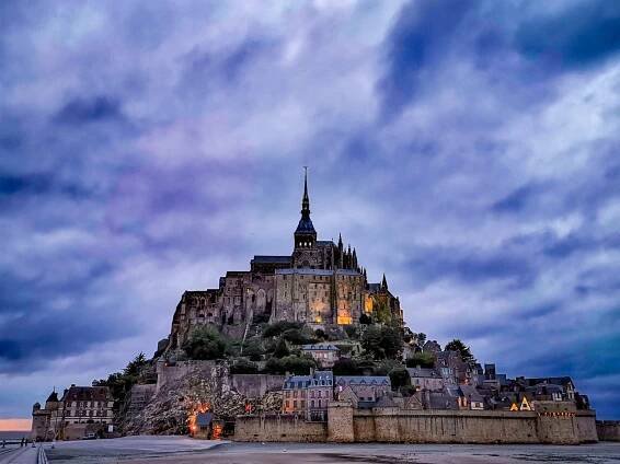 an old castle is lit up at night on top of a hill in the middle of town