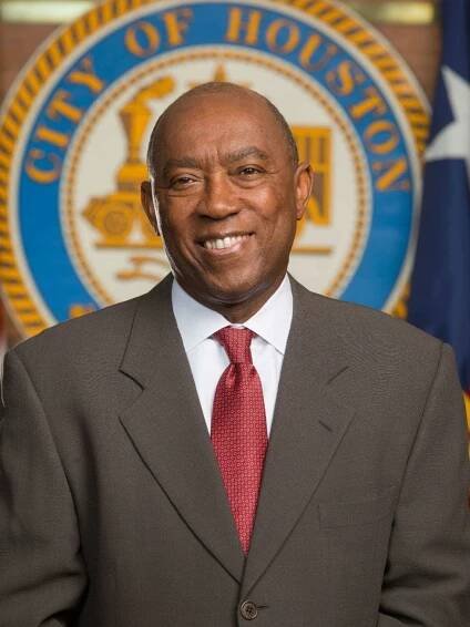 A man in a suit and tie stands in front of a city of houston seal