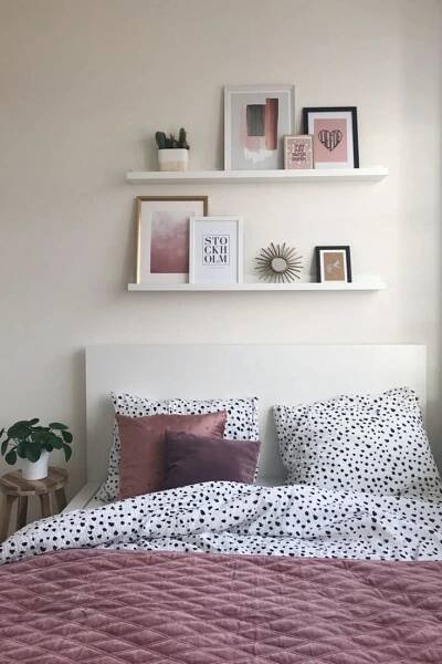 a bed with pink sheets and pillows in a bedroom next to a wall mounted shelves