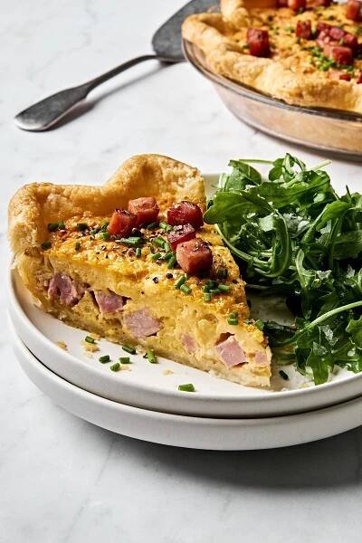 a slice of Quiche Lorraine made with eggs, ham, spices, cream and Gruyère served with a simple green salad
