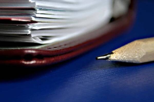 A pencil in the foreground and a stack of papers in the back, blurred