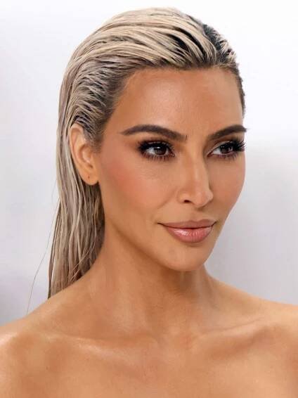 Kim Kardashian with slicked-back platinum hair, bronzed skin, nude pink lipstick, blush, and mascara