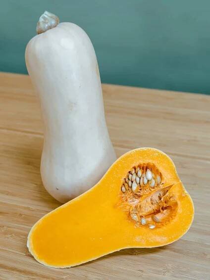 Two butternut squash, with one of them cut open to show the orange flesh inside.