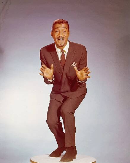 Sammy Davis Jr. joyfully poses mid-dance in a tailored suit and tie, exuding charm and energy