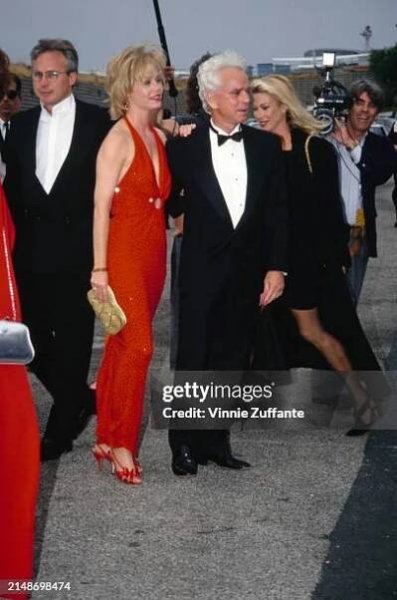 American actress Susan Dey, wearing a full-length red halterneck dress with a plunging neckline, and her husband, American film producer Bernard...