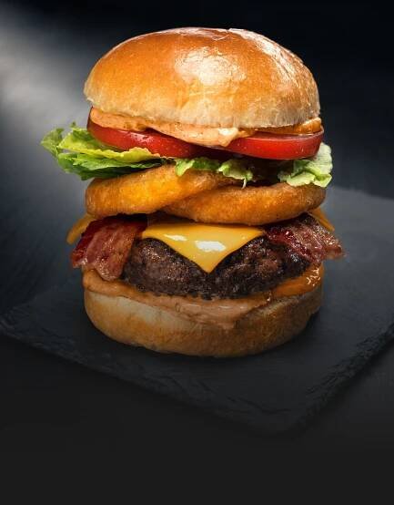 Juicy burger topped with onion rings, cheese, lettuce, and tomato on a soft bun.