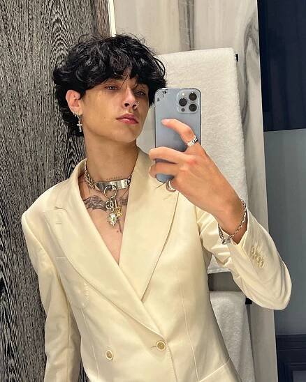 Selfie of a young person wearing a cream-colored blazer and jewelry.