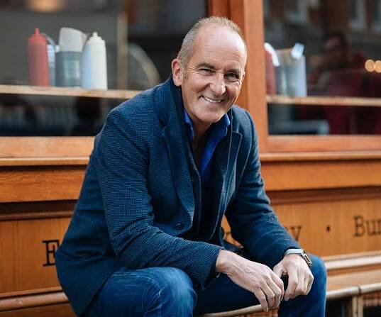 Kevin Mccloud smiling sitting on a bench