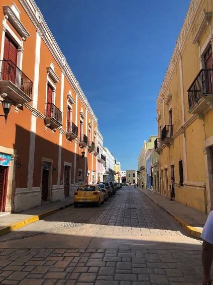 A man is walking down a cobblestone street between two buildings