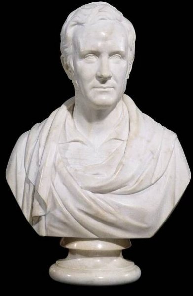 A marble bust of a male figure  wearing a robe in the classical style, attached to a polished marble socle. 