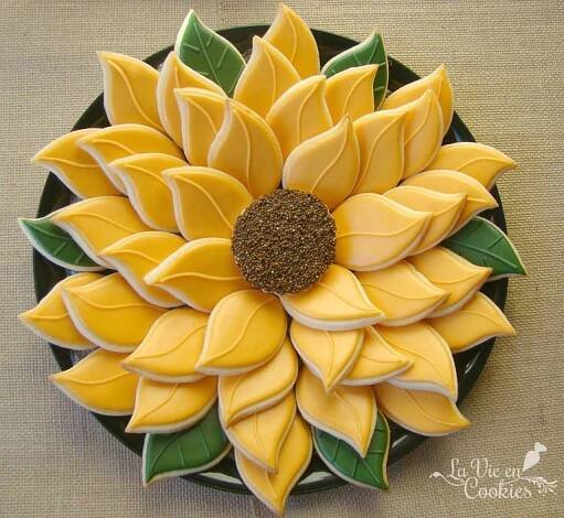 a sunflower shaped cookie sitting on top of a black plate covered in icing