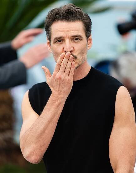 Person on red carpet in sleeveless black shirt blowing a kiss, surrounded by blurred background and others