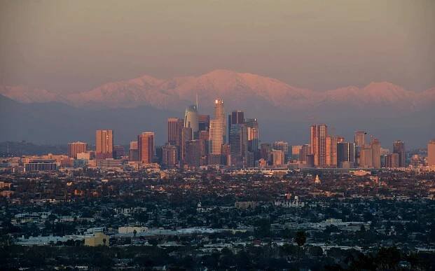 This photo shows a view of the downtown Los Angeles skyline with the snow-covered San Gabriel Mountains in the background as the sun sets on February 7, 2019.