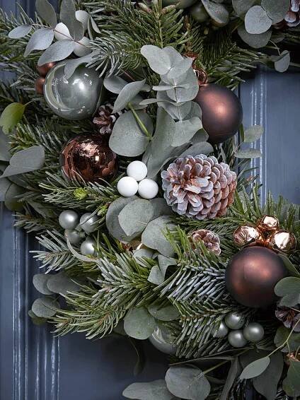 a christmas wreath with pine cones, berries and evergreen leaves on a blue front door