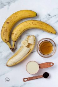The ingredients needed to make banana popsicles, including ripe bananas, on a marble countertop