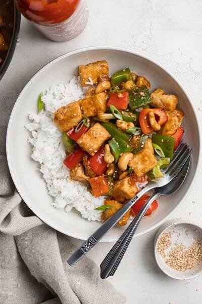 kung pao tofu on a plate over rice, with sesame seeds on top