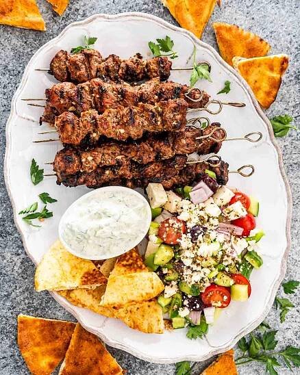 lamb souvlaki on a platter with tzatziki sauce, greek salad and pita bread.