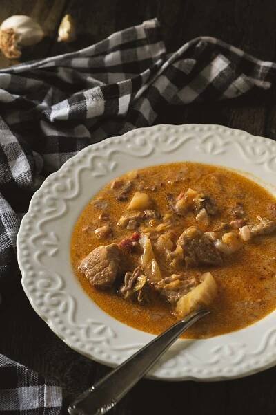 A shallow and ornate white bowl full of segedinsky gulas and tender pork shoulder pieces with sauerkraut.
