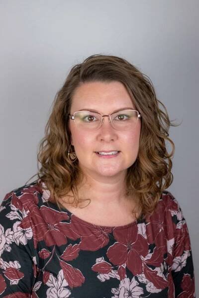 A woman wearing glasses and a floral shirt is smiling for the camera.