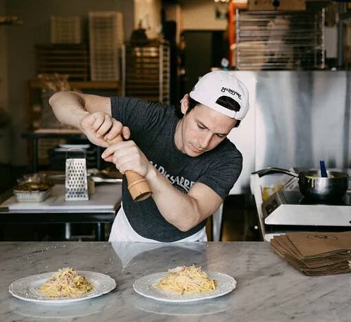 Man seasoning pasta on plates with a pepper grinder.