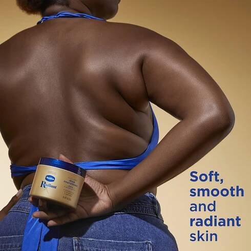 Vaseline Intensive Care Cocoa Radiant Lotion held by a woman with rich, dark skin, showcasing the product's hydrating effect. She wears a vibrant blue top and denim, with text promising soft, smooth, and radiant skin.