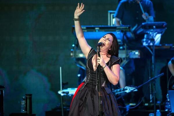 Singer passionately performing on stage in a black, sleeveless dress, holding a microphone, with one arm raised