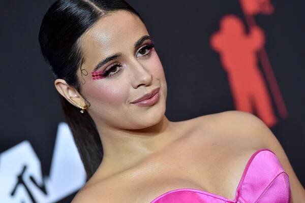 Camila Cabello wears a long, center-parted ponytail and bold makeup with colorful dots on the corners of her eyes