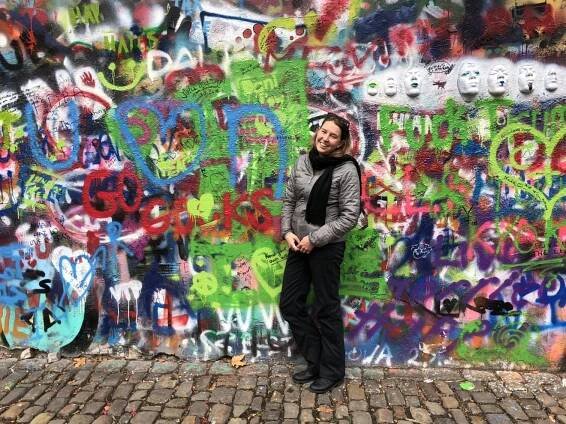 Riley standing in front of the colorful graffitied John Lennon Wall in Prague