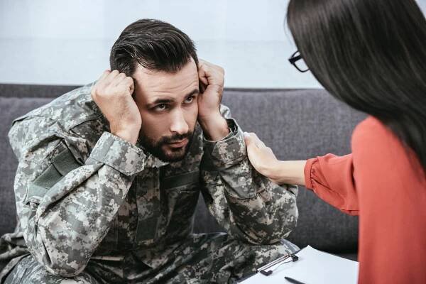 Man wearing military uniform grips head while a VA PTSD lawyer Texas talks to him with a helping hand on his shoulder