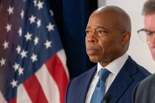 Mayor Eric Adams photographed at a news conference while wearing a dark suit and tie.