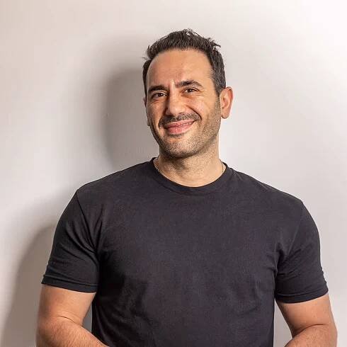 Smiling man in black t-shirt leaning against white wall