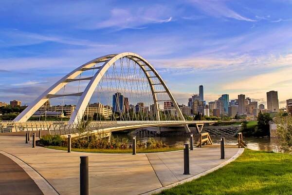 Modern arch bridge with city skyline in the background at sunset
