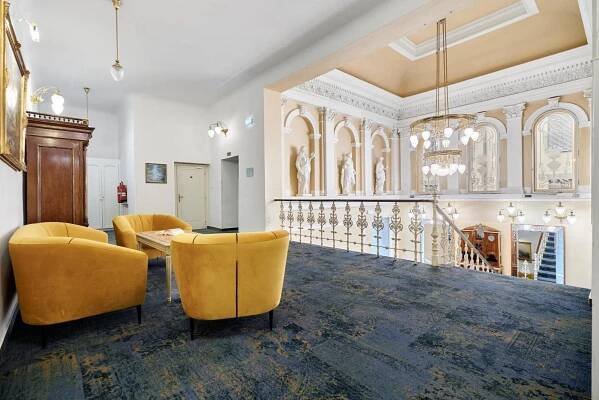 a lobby with yellow chairs and a table and a staircase at Hotel Maxim in Mariánské Lázně