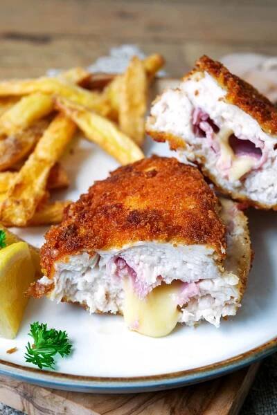 Hähnchen-Cordon-Bleu angeschnitten mit Pommes auf einem Teller.