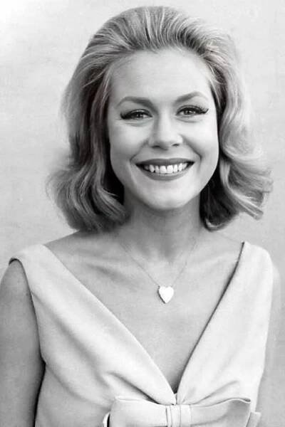 a black and white photo of a smiling woman with blonde hair wearing a bow tie