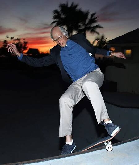 Tony Hawk rides a skateboard while dressed as Larry David in October 2022