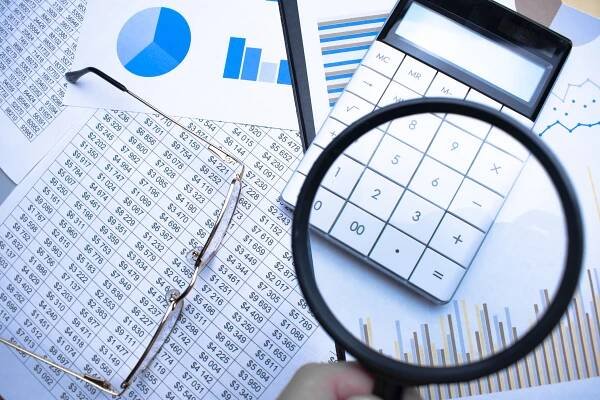 Close-up Of Businessperson Checking Bills With Magnifying Glass