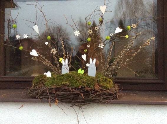 a window with some branches and white rabbits in the center, on top of a moss covered ledge