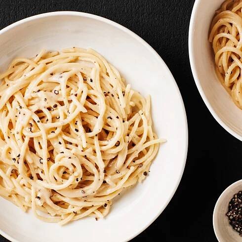 Two wide shallow bowls of cacio e pepe with a small pinch bowl of freshly cracked black pepper on the side.