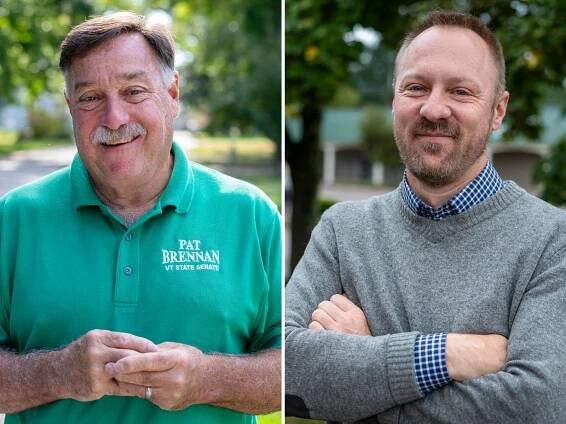 Two men are posing outdoors. One wears a green polo with text and the other wears a gray sweater over a checkered shirt. Both smile and stand in a tree-lined setting.