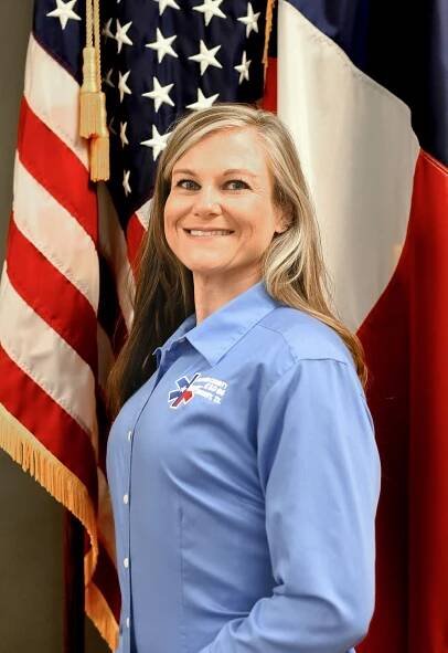 A woman in a blue shirt is standing in front of of an American flag.