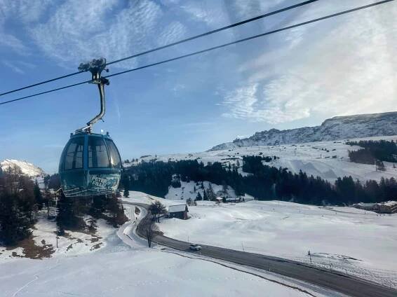A snowy day on Alpe di Siusi in the Dolomites in Italy. A blue gondola car passes above the snow and the road.