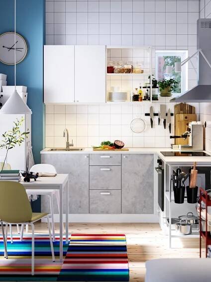 A kitchen with ENHET kitchen cabinets, a table and chairs on a colourful rug and a white pendant lamp above.